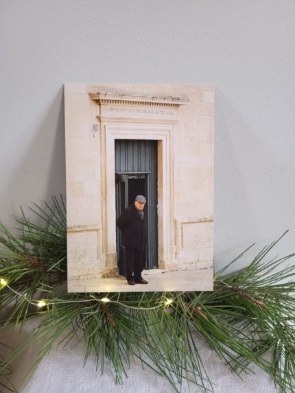 Carte postale représentant un homme âgé debout devant une porte ancienne en pierre claire à Martina Franca